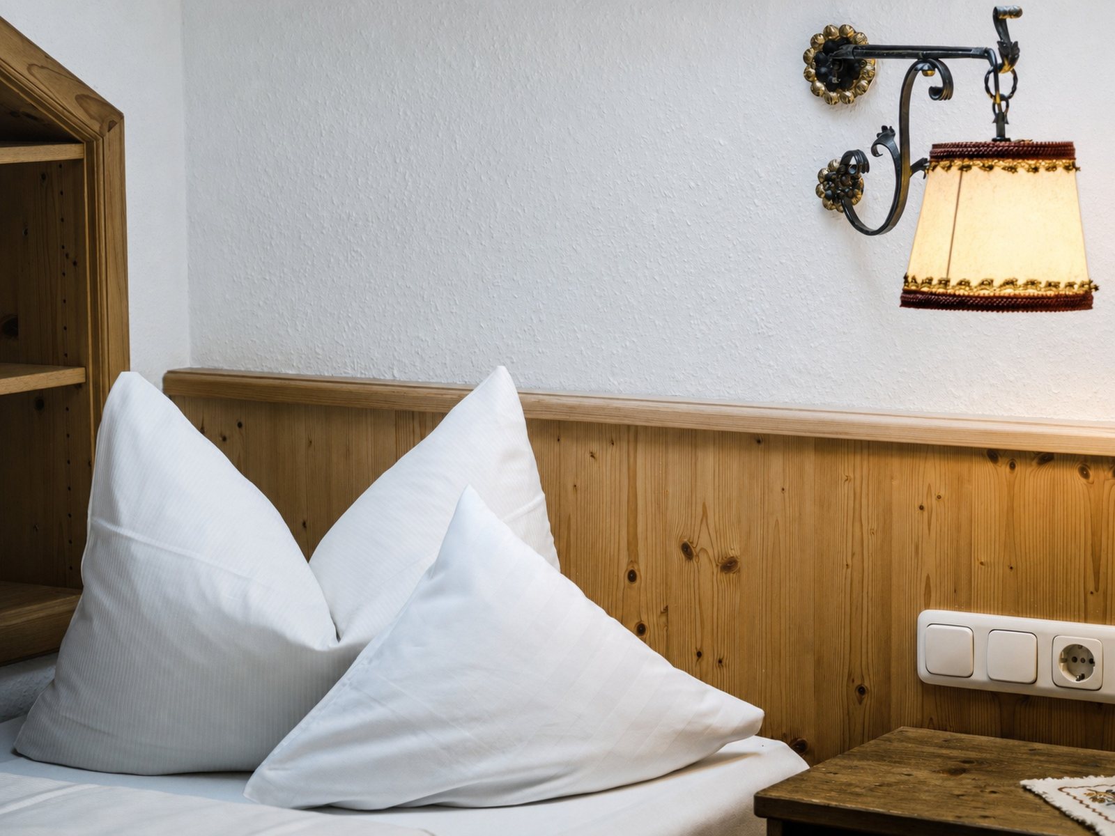 The same corner with a white wall and white pillows, the wood keeps its tone, the lampshade still glows warm, the picture is a little brighter.