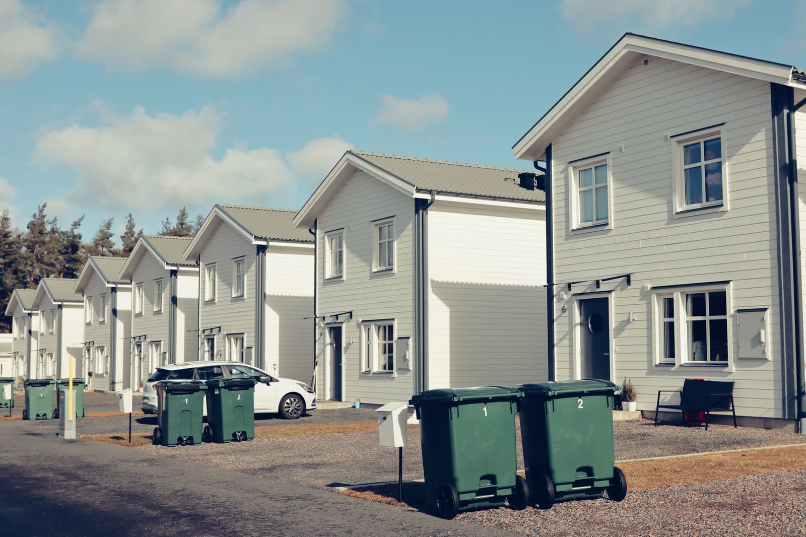 Row of houses with wheelie bins by the door and a parked car.